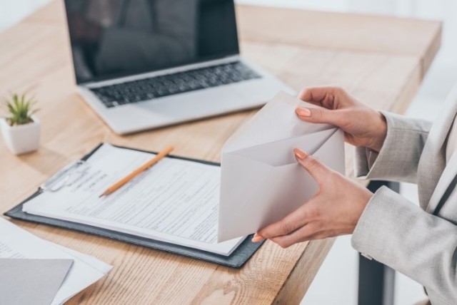 businesswoman holding open envelope in hands at workspace