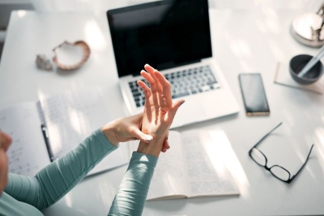Woman with hand pain massaging during work on a laptop