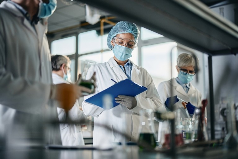 scientist taking notes while working with her colleagues in laboratory