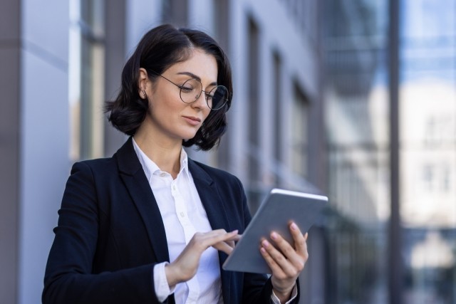 woman in a suit looking at an ipad outside office building
